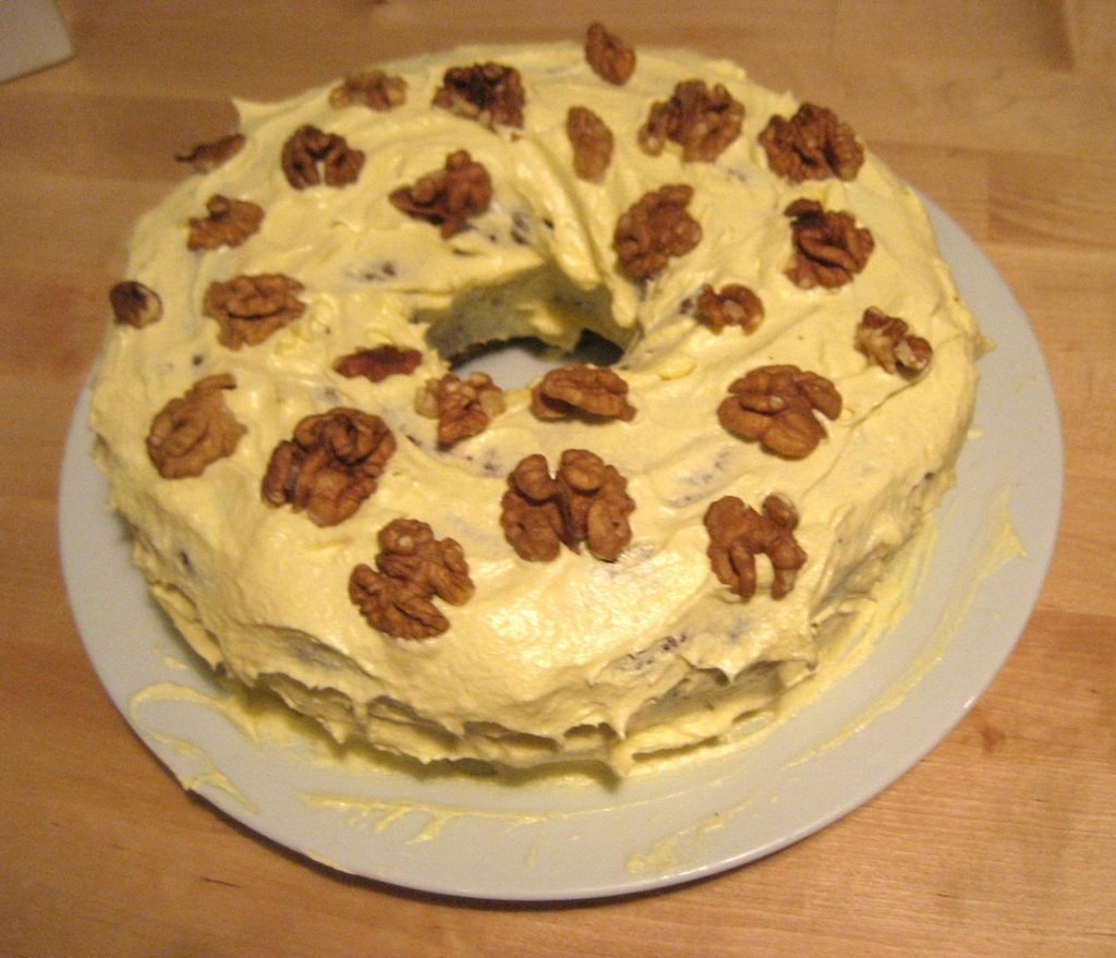 Ring shaped cake with cream cheese frosting topped with walnut halves