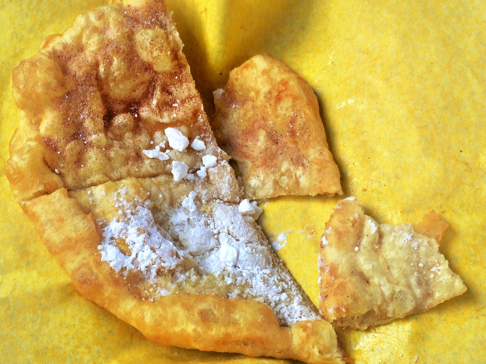 Torn fry bread dusted with powdered sugar on a yellow plate
