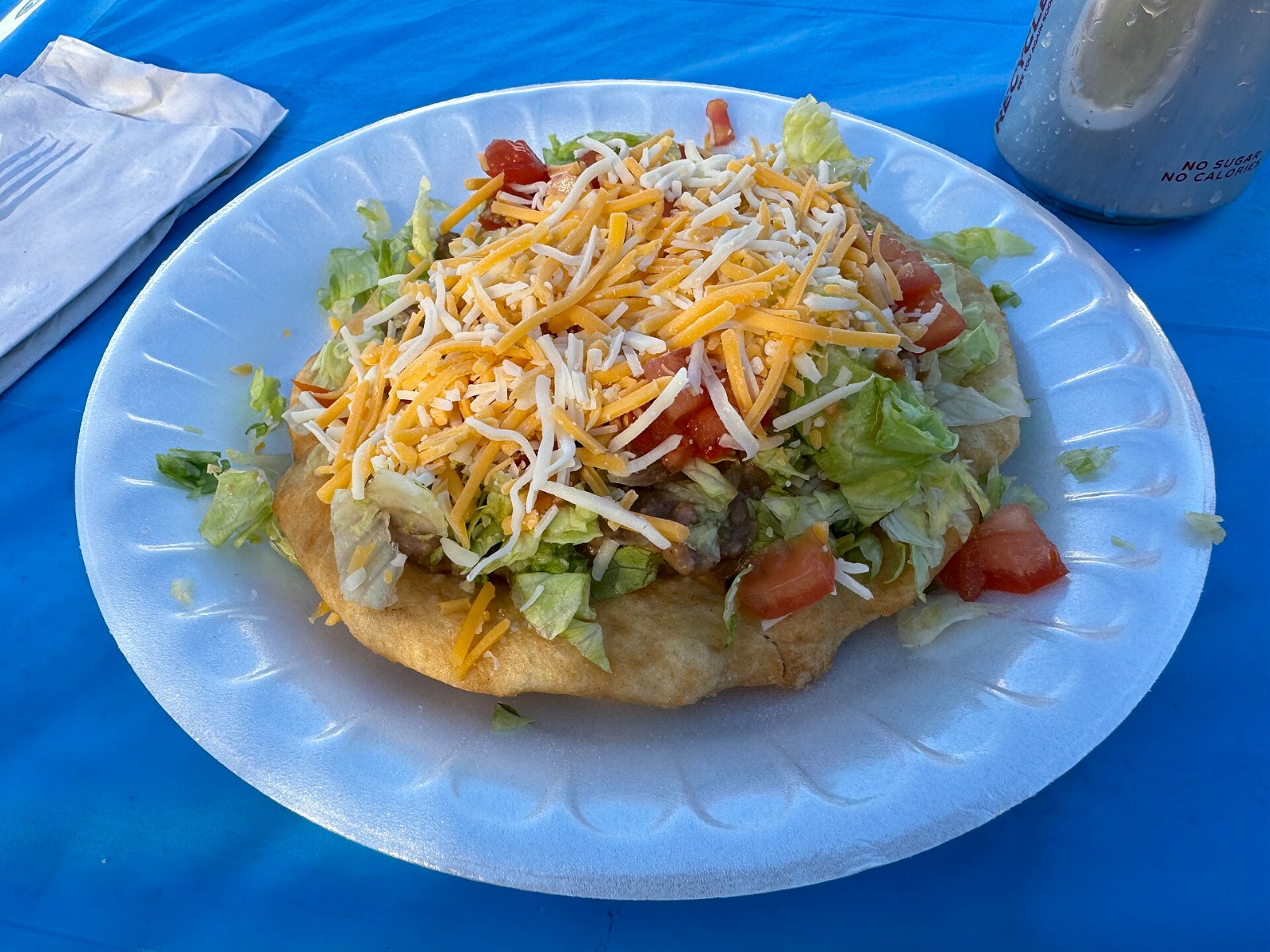 Indian taco piled with lettuce, tomato and shredded cheese on a paper plate