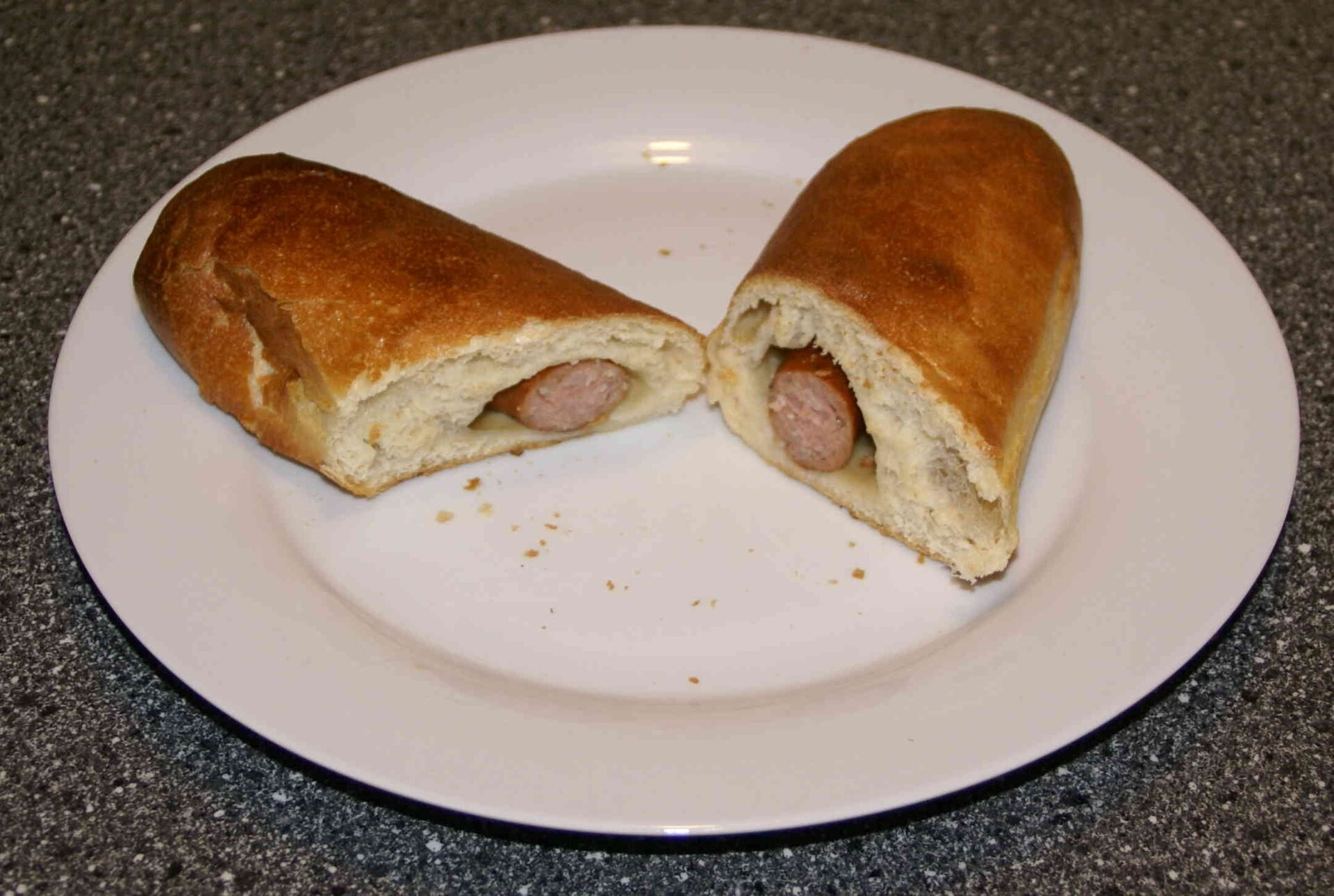Hot dogs baked in soft bread dough, cut open on a white plate