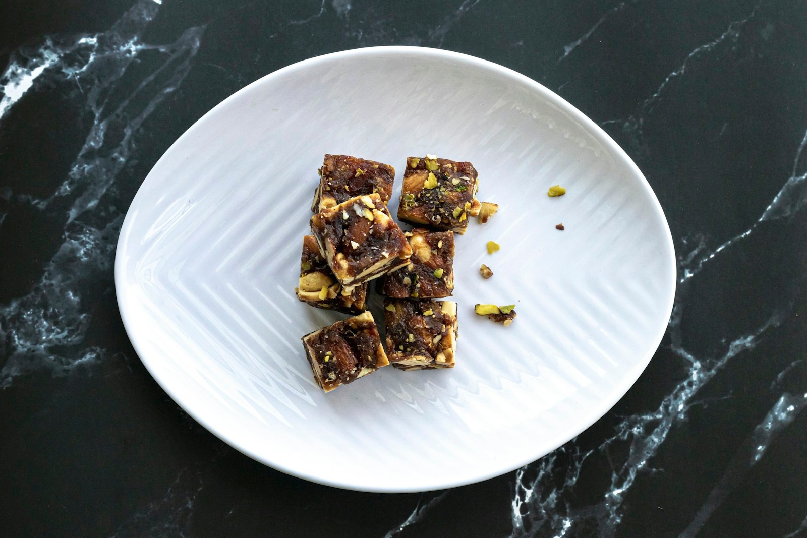 Small chocolate fudge squares with pistachios on a white plate