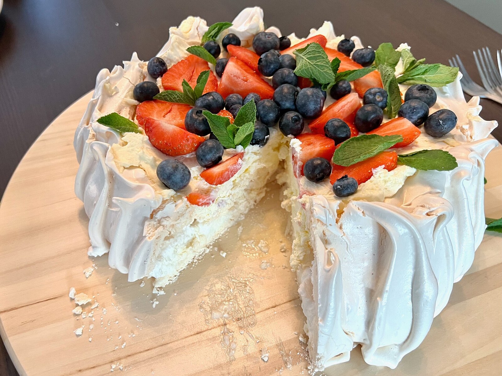 Christmas pavlova inspiration: a classic pavlova topped with cream, strawberries, blueberries and mint, one slice cut