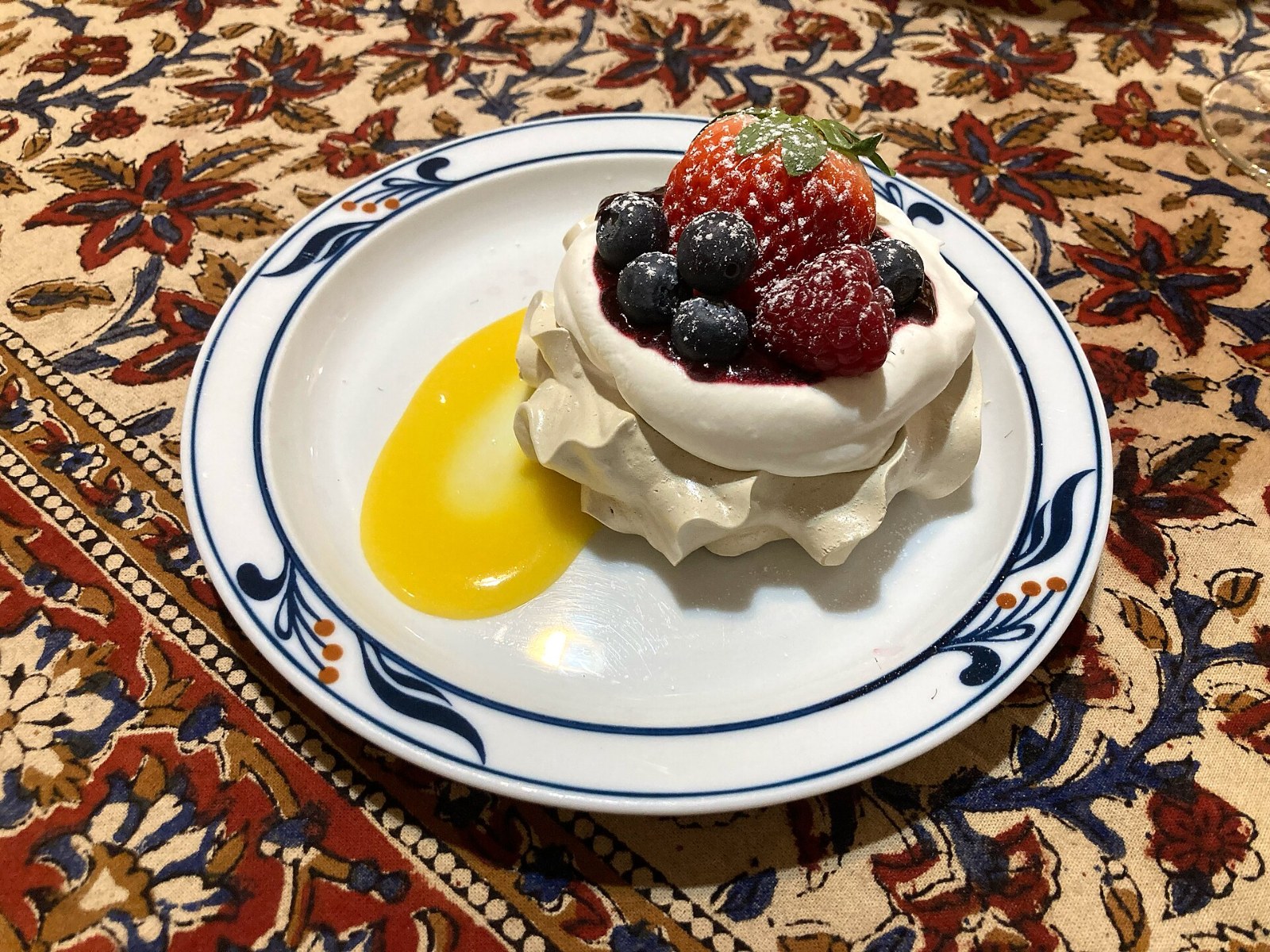 A small meringue nest with berries and a spoon of lemon curd on a plate