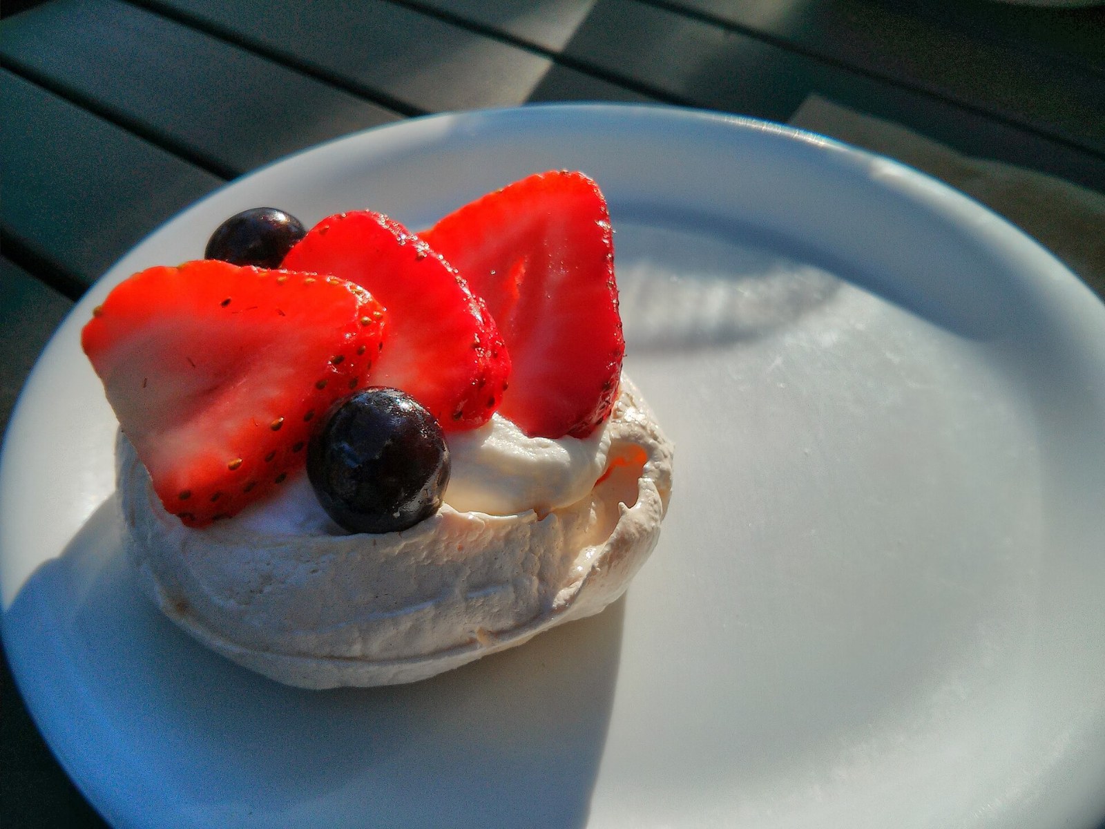 A mini pavlova nest filled with cream, strawberries and a blueberry