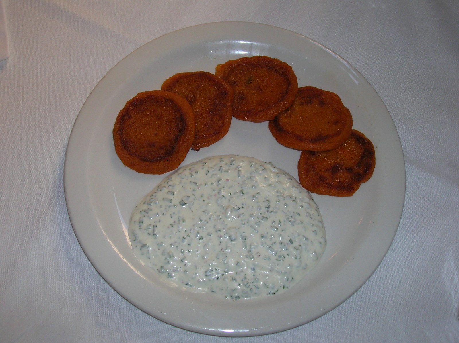 Golden orange sweet potato pancakes on a plate with a creamy dip