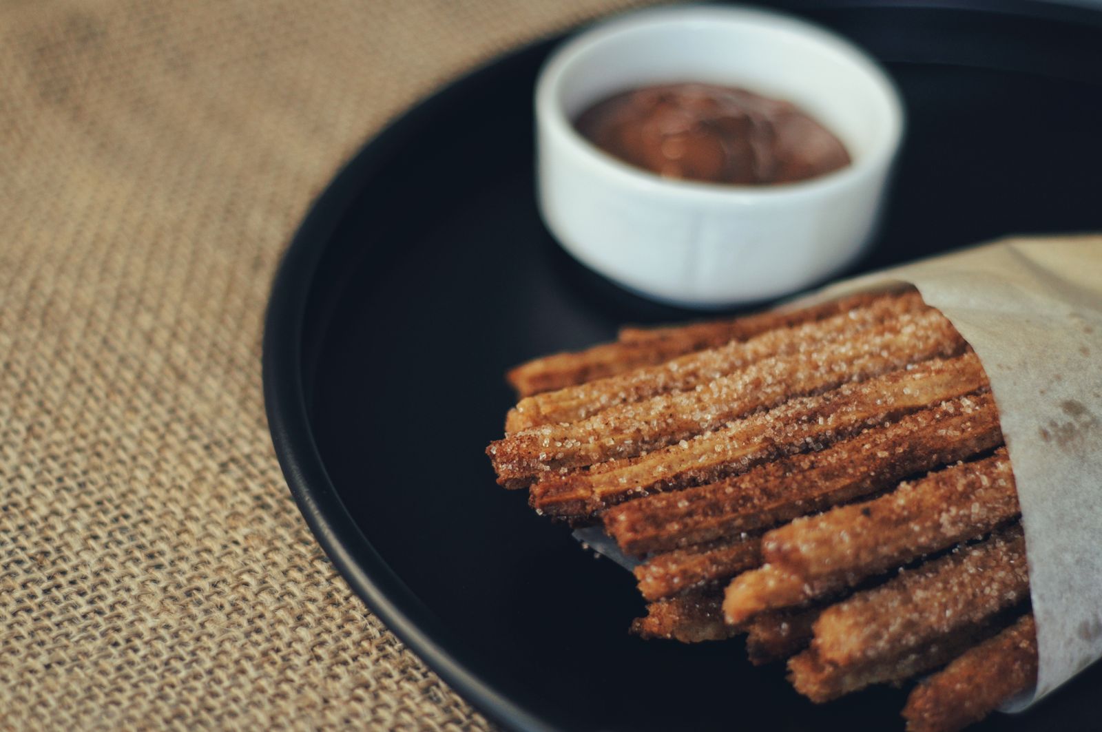 Cinnamon sugar churros in a paper cone with chocolate dip