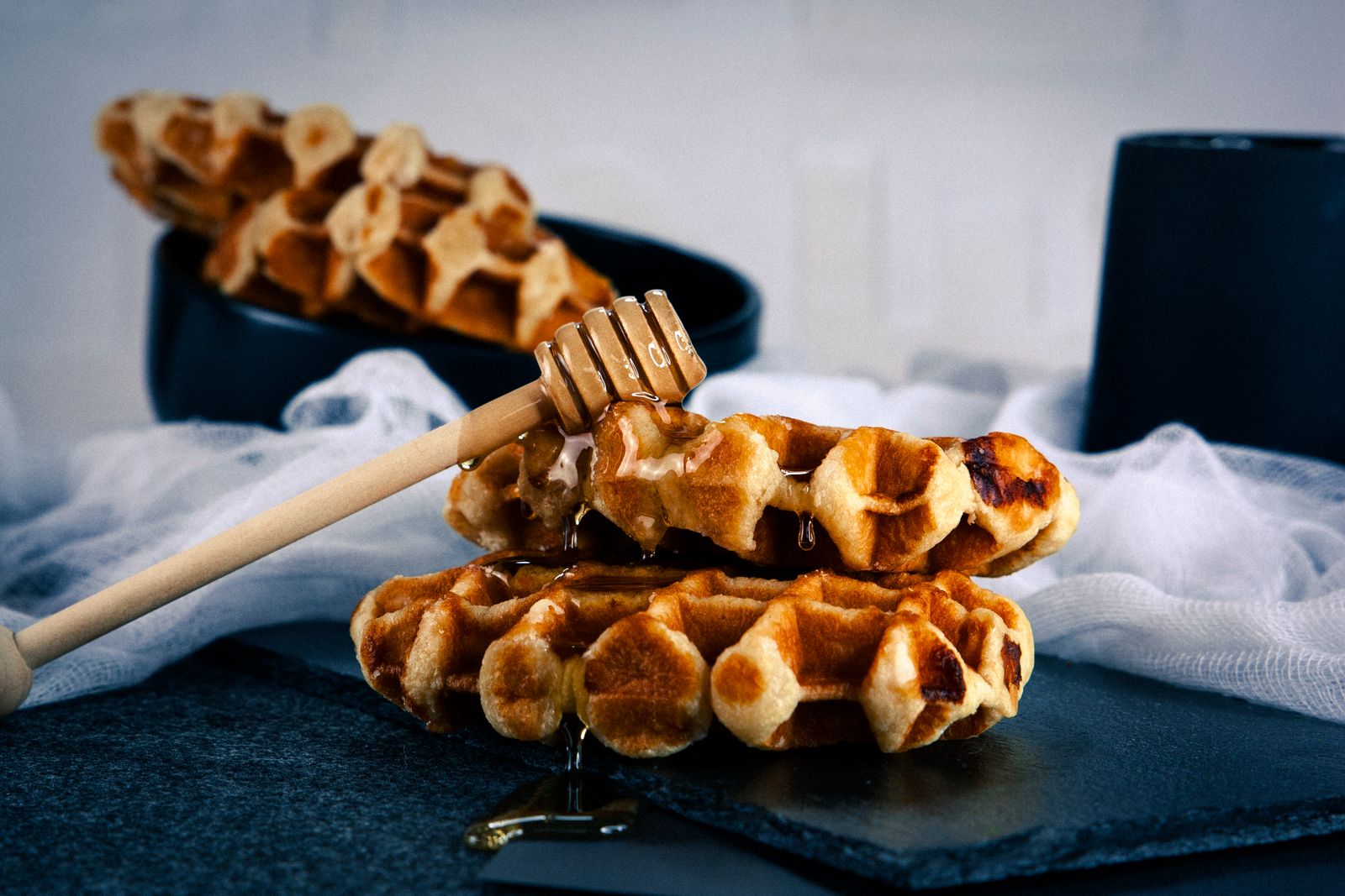Golden waffles stacked with a wooden honey dipper