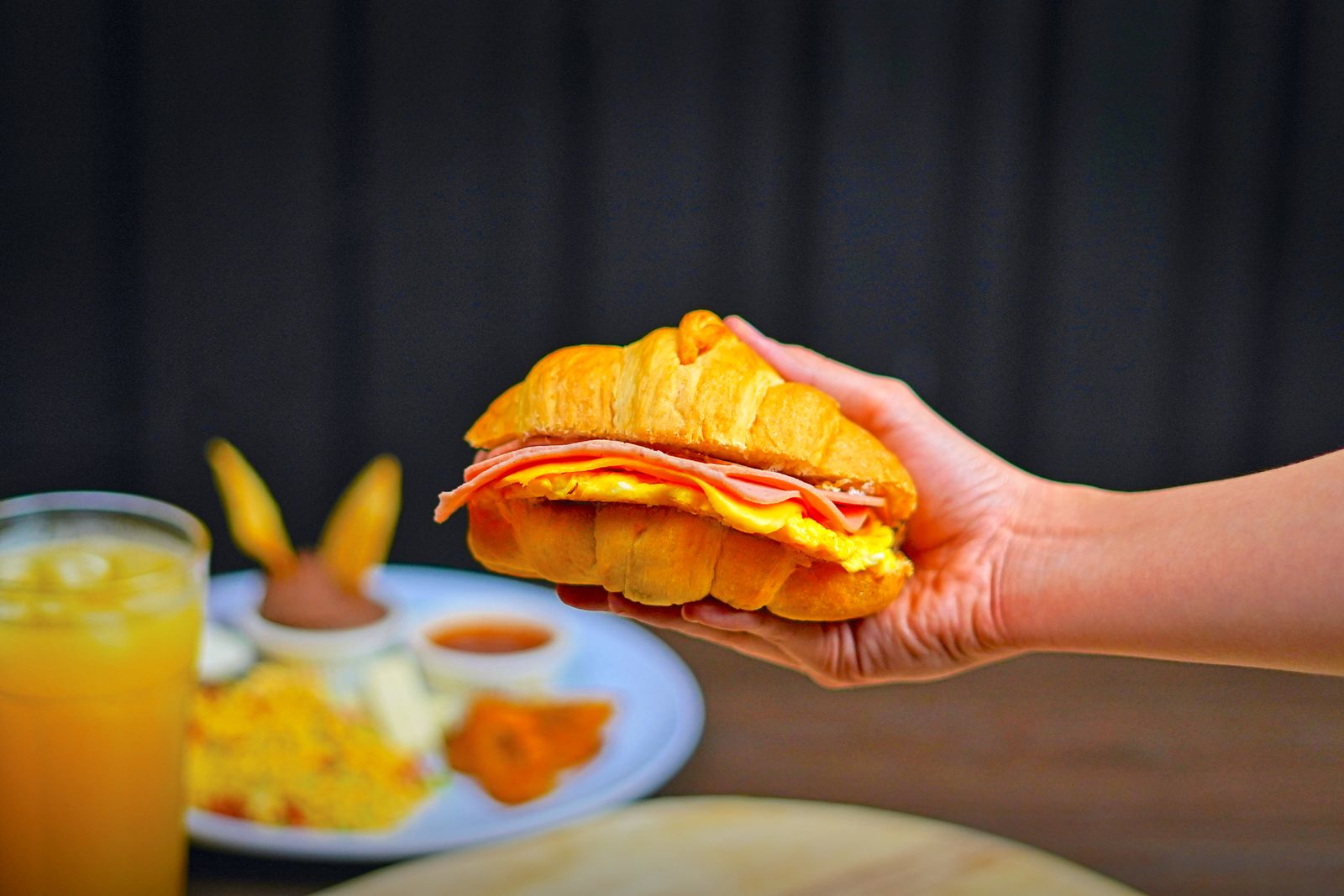 Breakfast sandwich with egg, ham and cheese held in hand