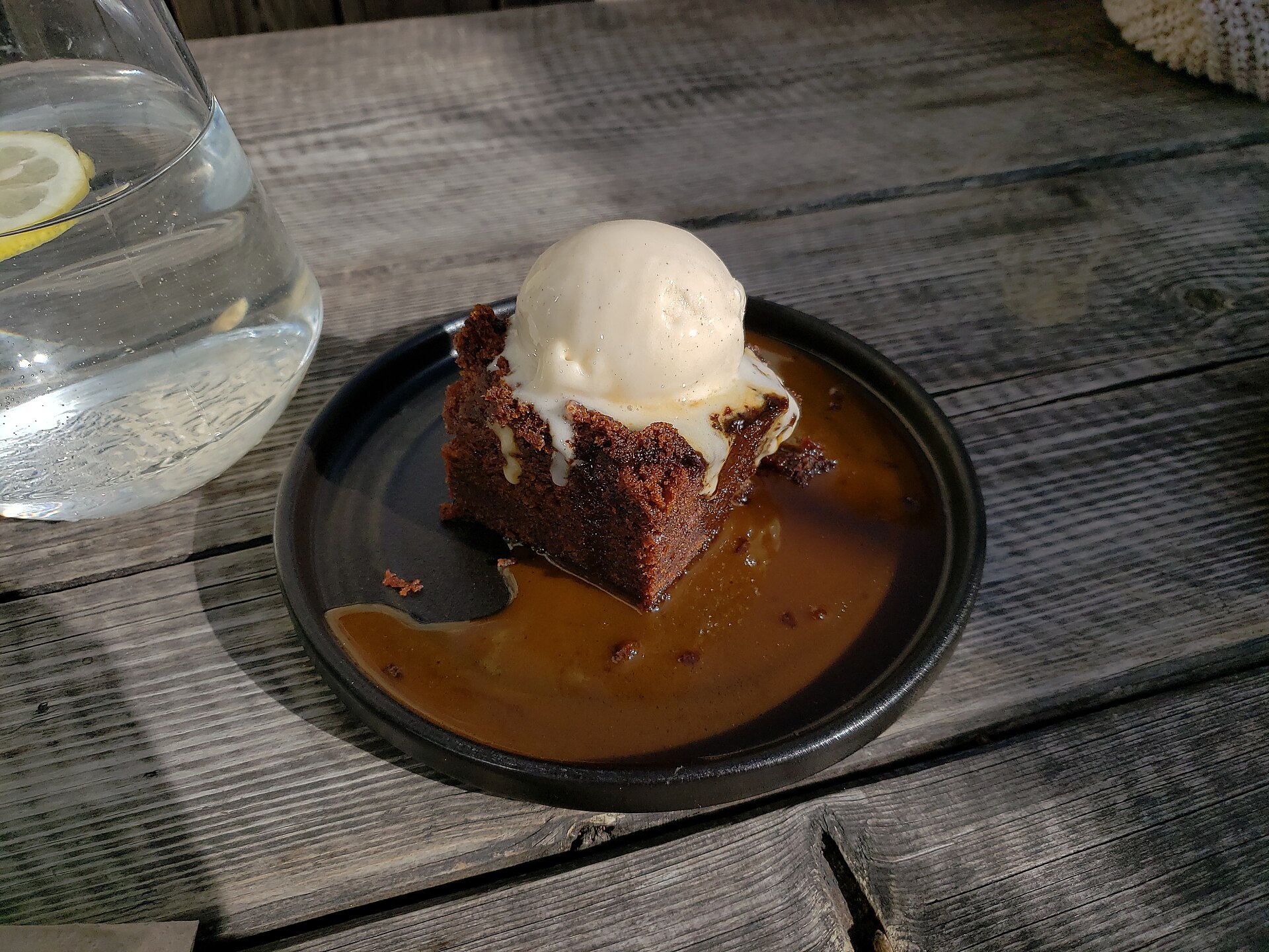 Warm date pudding with ice cream and sauce in a dark bowl