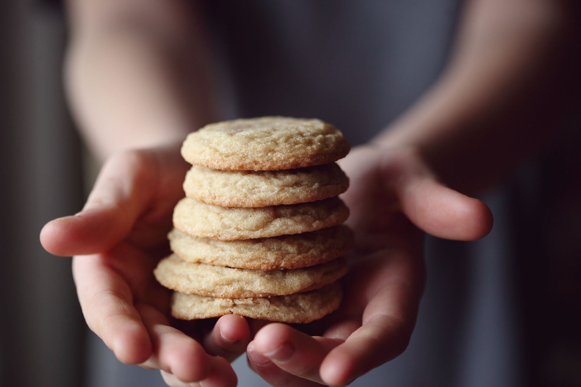 A stack of soft sugar-crusted cookies held in two hands