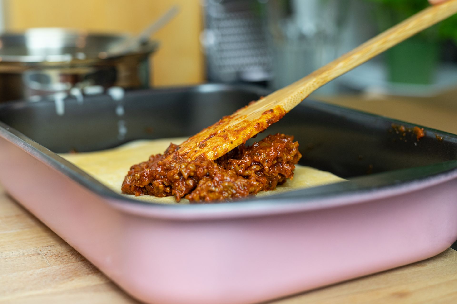 Spreading meat sauce over noodles in a large pan