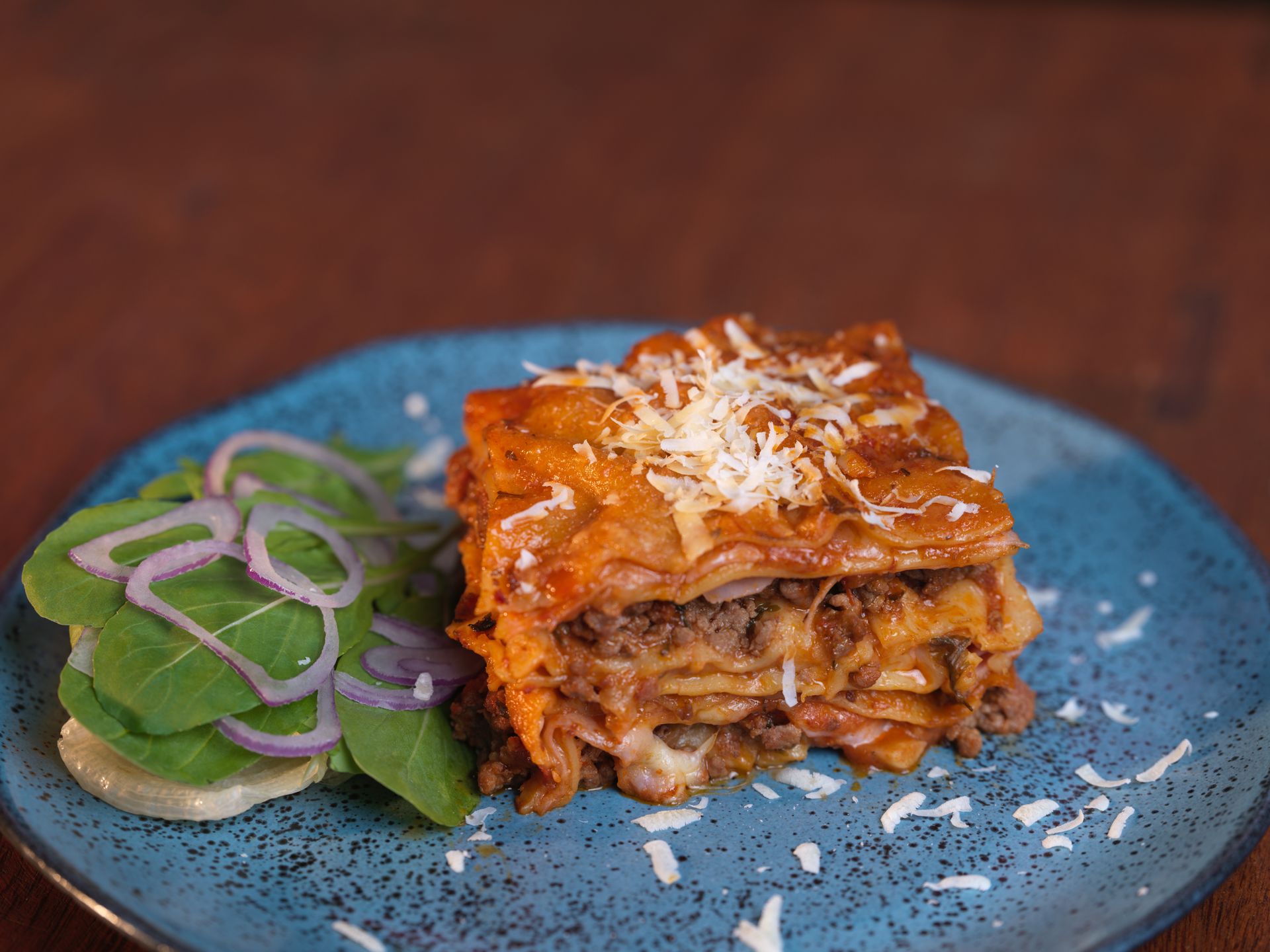 Lasagna slice with meat sauce and Parmesan on a blue plate