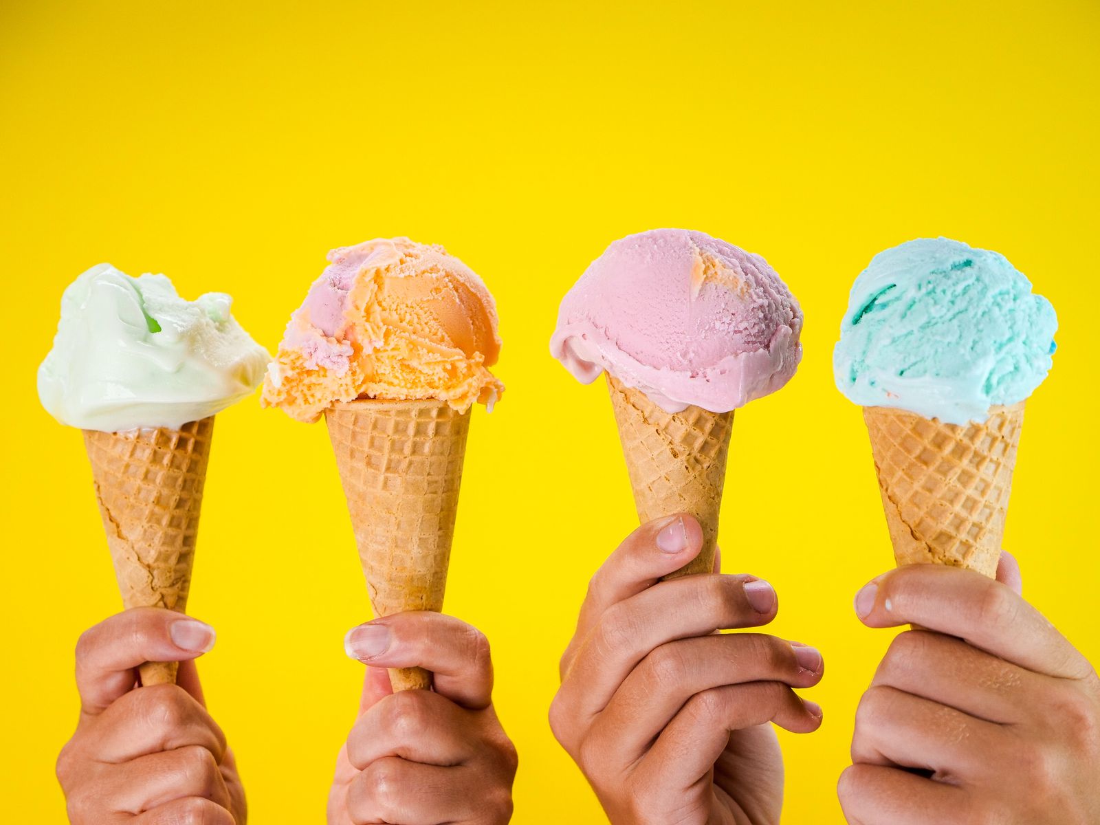 Four ice cream cones ready for eating against a yellow wall