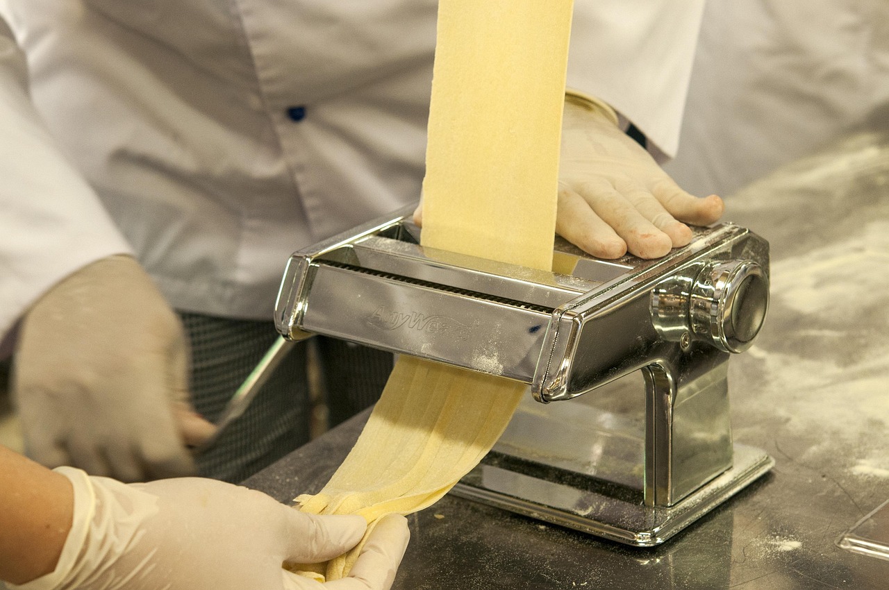 Fresh pasta sheet rolling out of a hand-crank machine