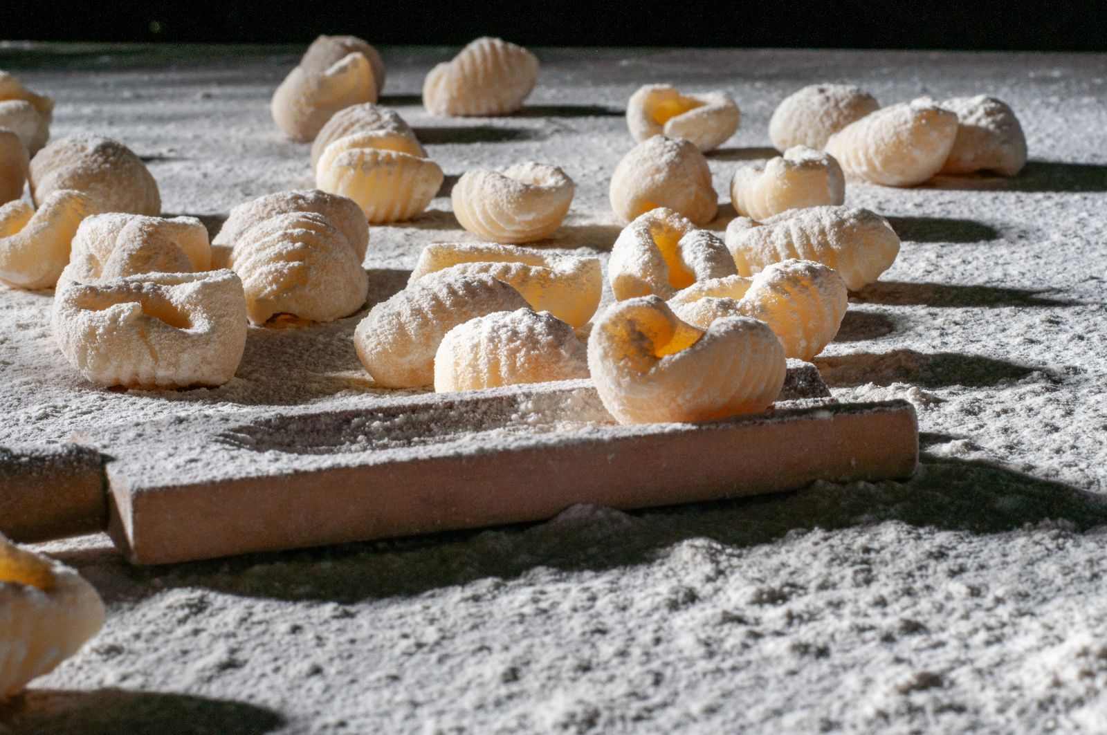 Little hand-shaped pasta on a wooden board with a rolling pin