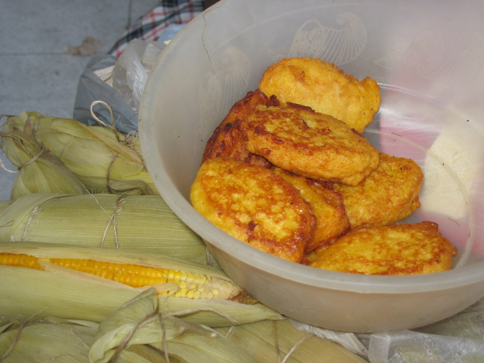 Golden corn fritters in a bowl with fresh corn husks