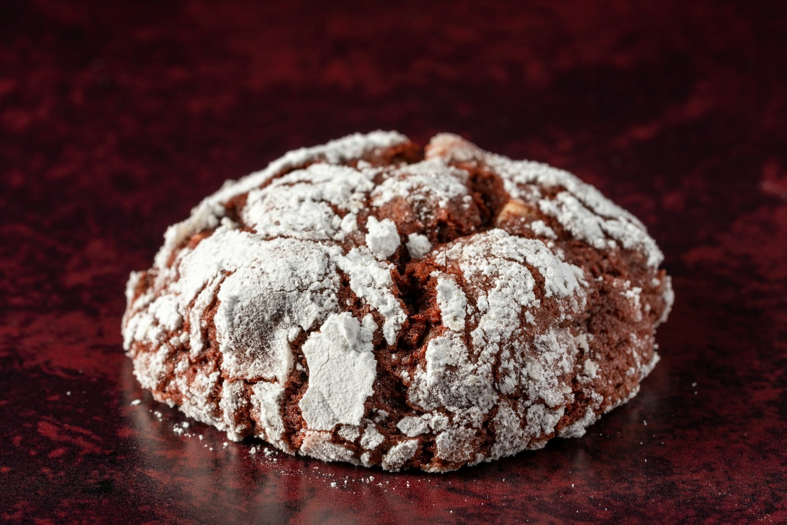 Double chocolate crinkle treat covered in powdered sugar on a dark red background