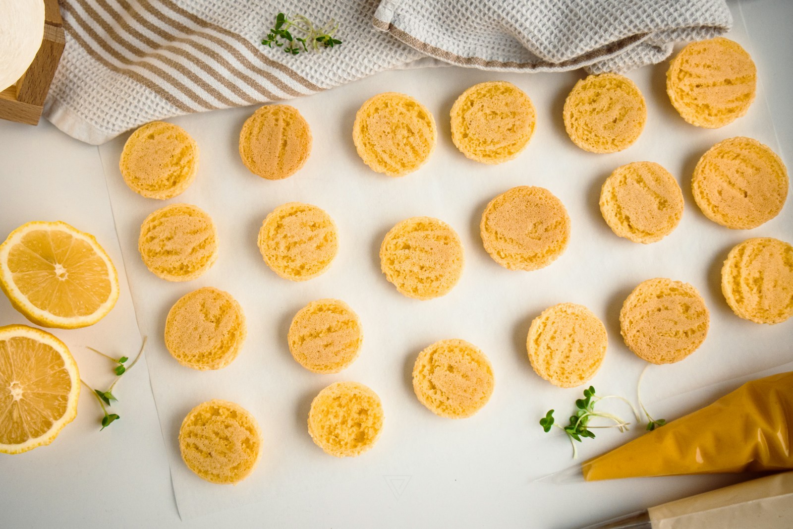 Golden lemon gooey butter cookies on parchment with fresh lemon halves