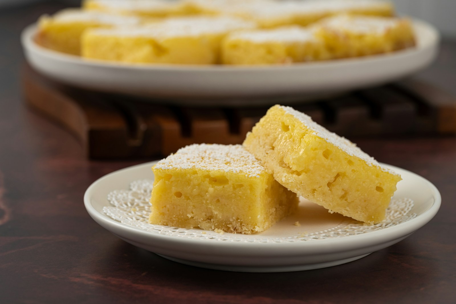 Squares of golden St. Louis gooey butter cake dusted with powdered sugar on a white plate