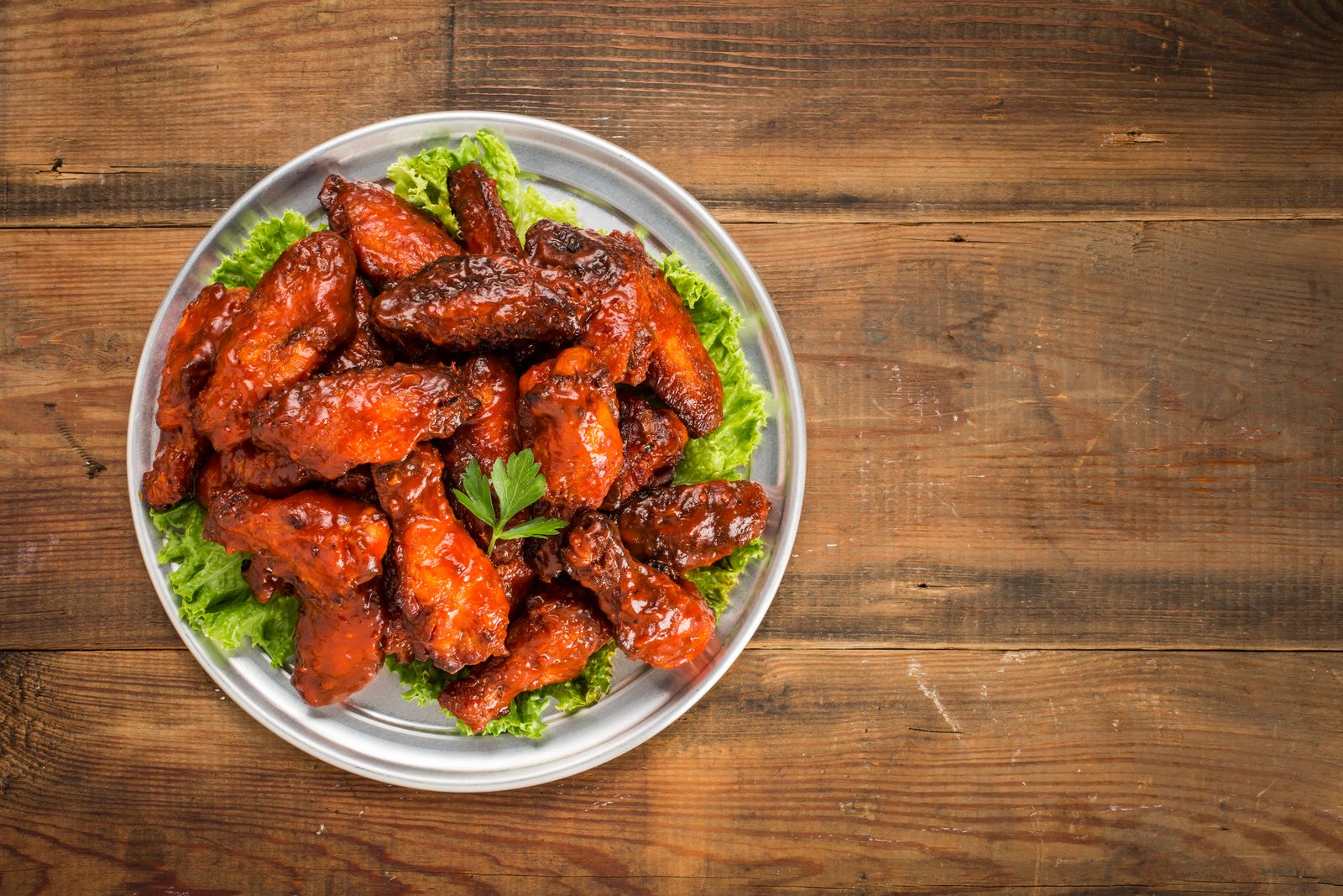 A bowl of saucy chicken wings on a wooden table
