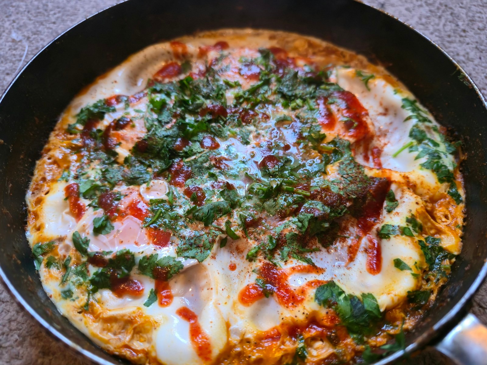 Eggs poached in a red tomato sauce in a skillet with fresh green herbs
