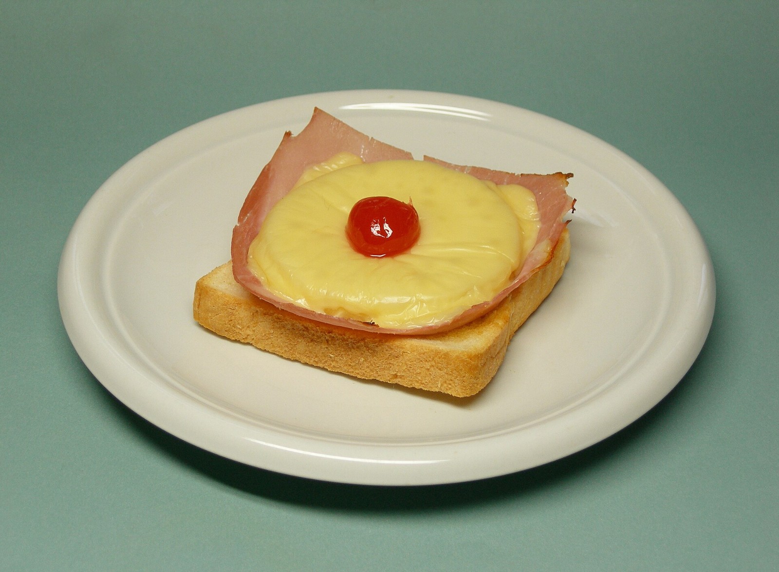 Toast topped with ham, a pineapple ring, melted cheese and a red cherry in the center