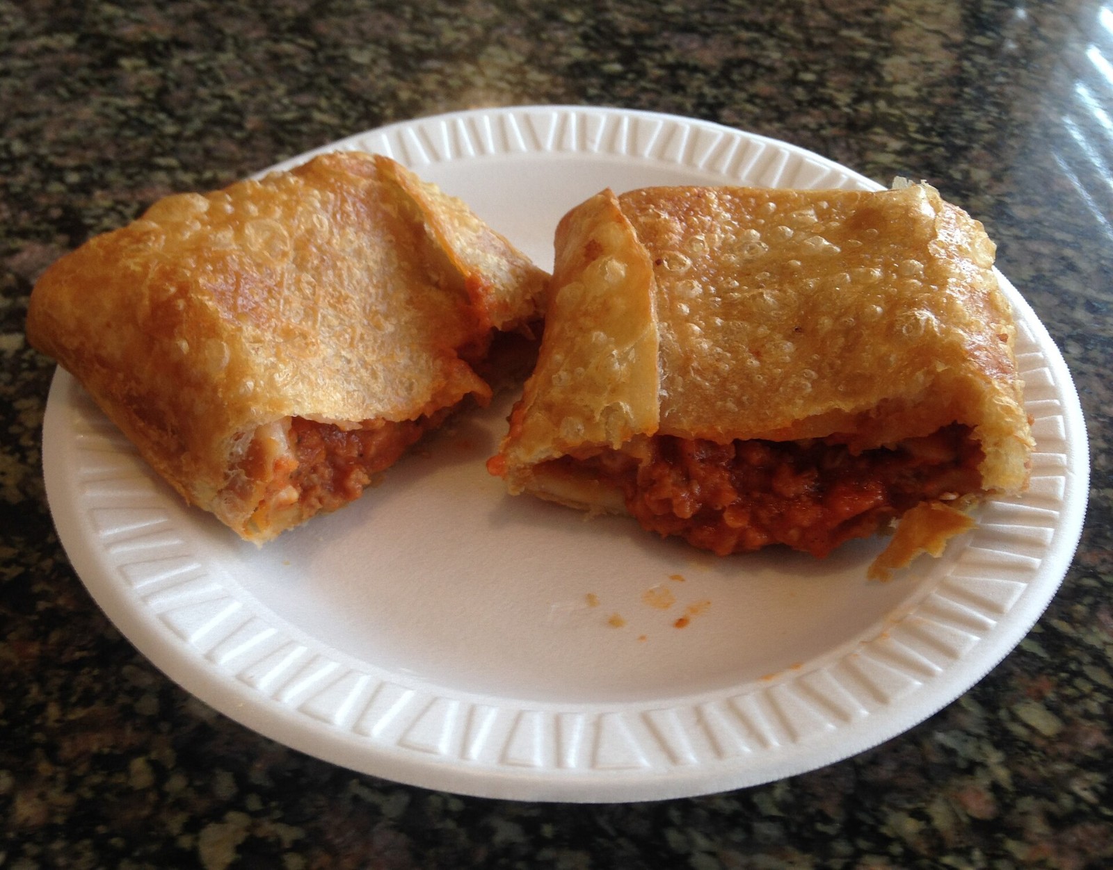 Golden fried pizza pocket cut open on a plate to show a saucy sausage and cheese filling