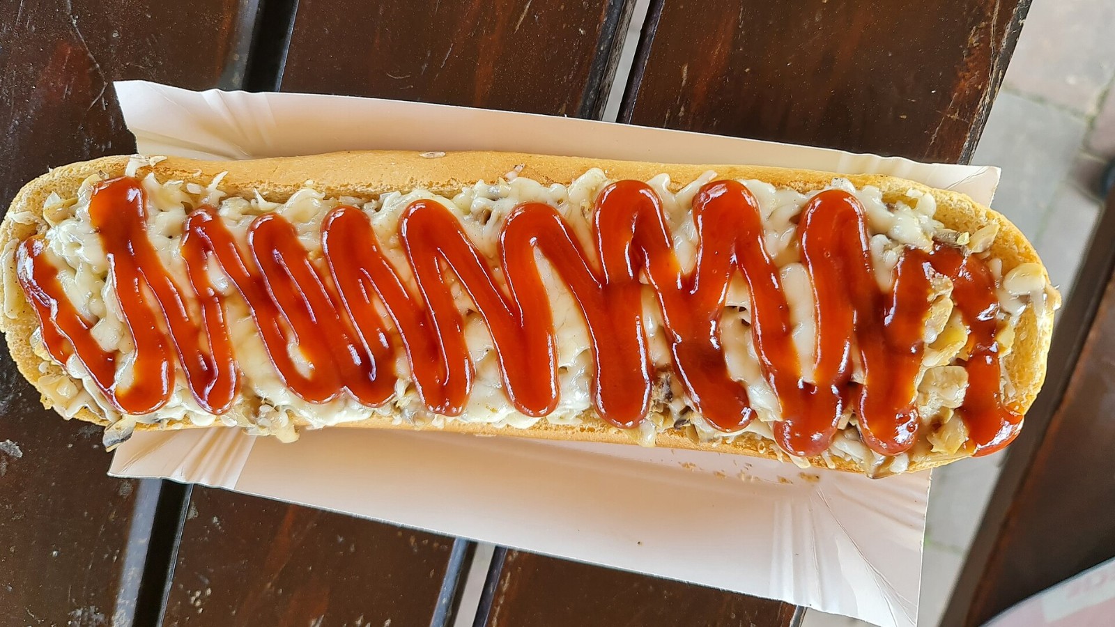 Long open-faced baguette topped with melted cheese, mushrooms and a zigzag of ketchup