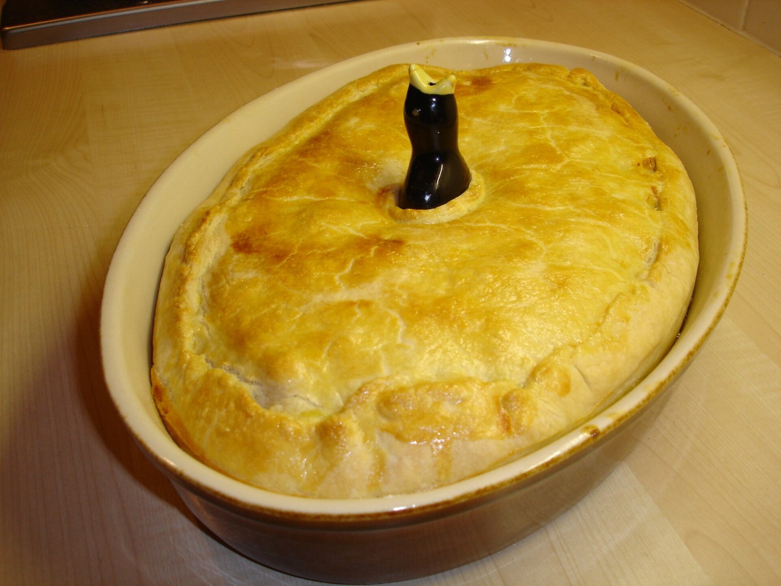 A golden pie with a ceramic pie bird poking through the crust