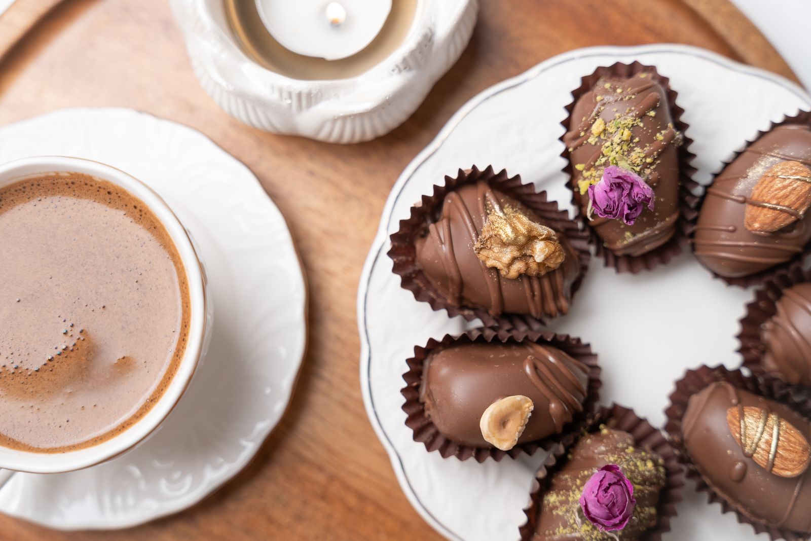 Chocolate-dipped stuffed dates decorated with pistachios next to coffee
