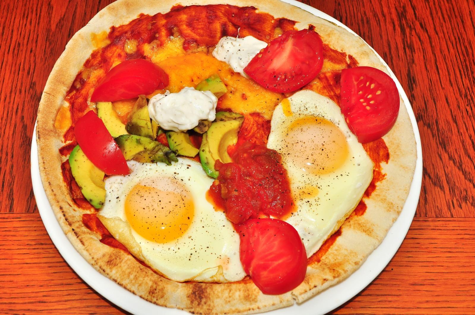 Breakfast pizza topped with sunny side up eggs and tomatoes