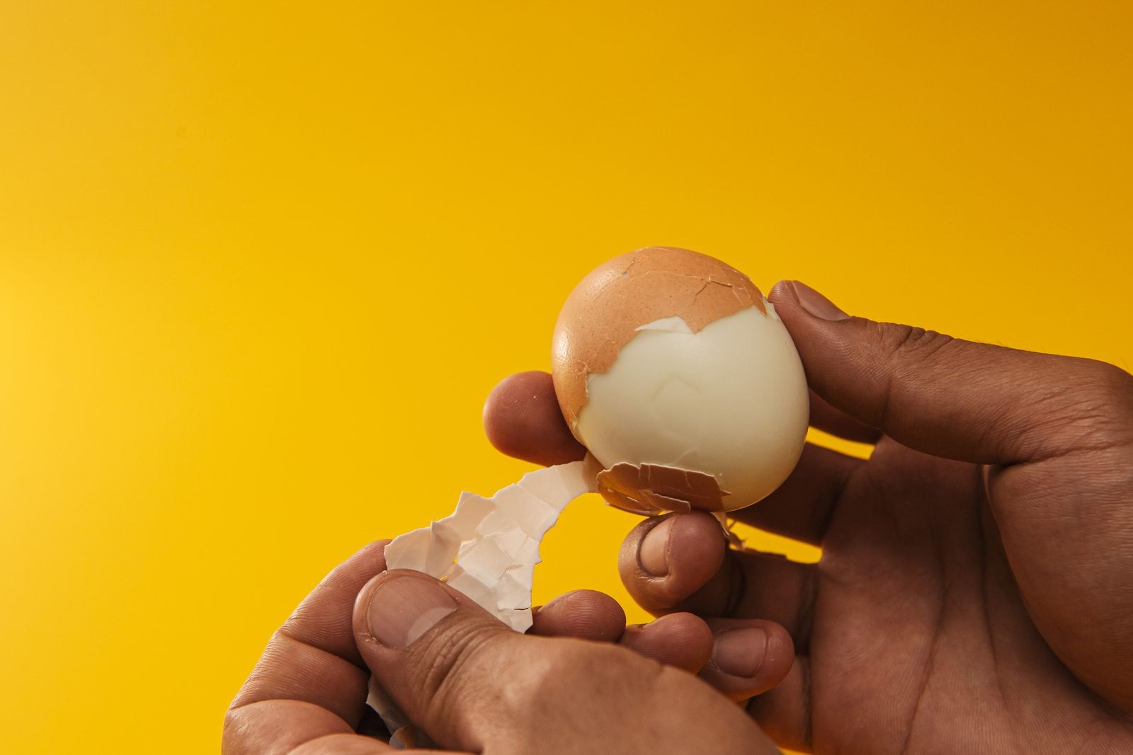 Egg hacks: hands peeling a boiled egg in big clean pieces
