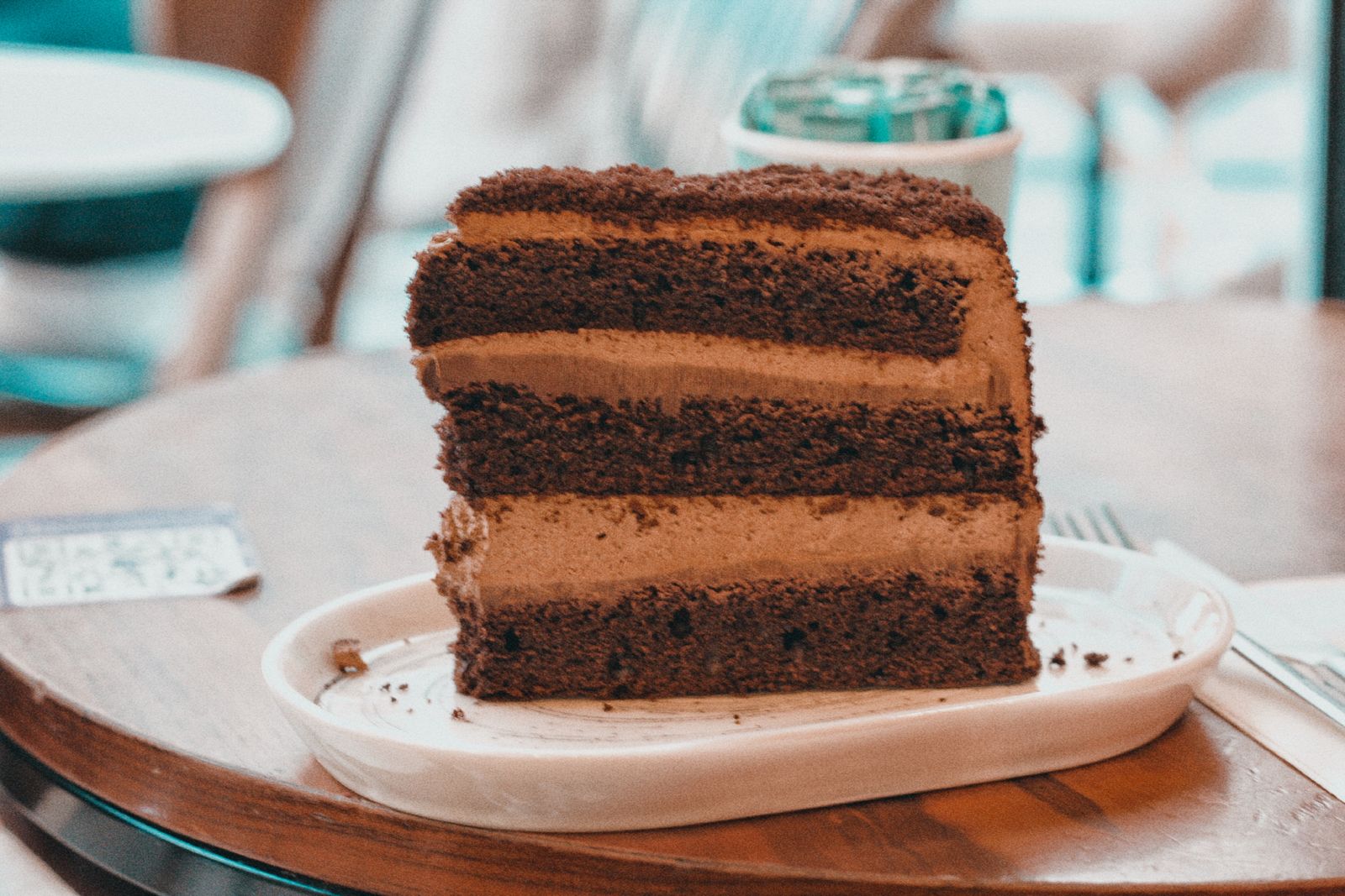 A tall, dark, fudgy slice with thick frosting on a plate