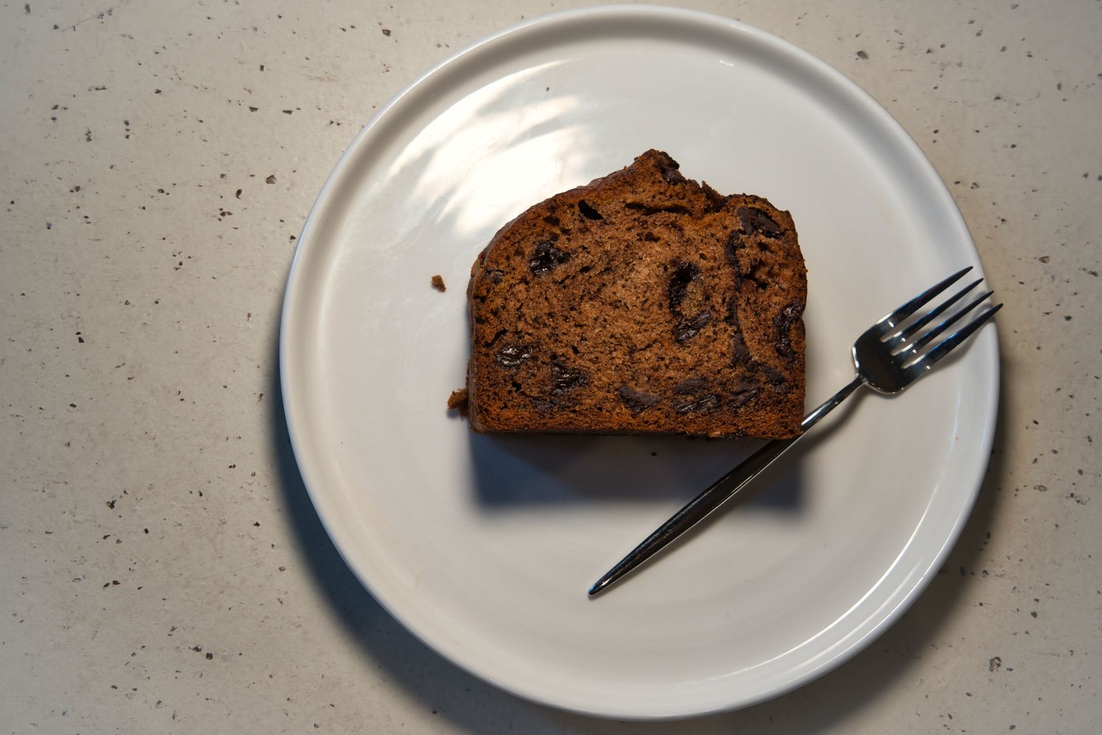 A slice of zucchini snack loaf with chips on a white plate