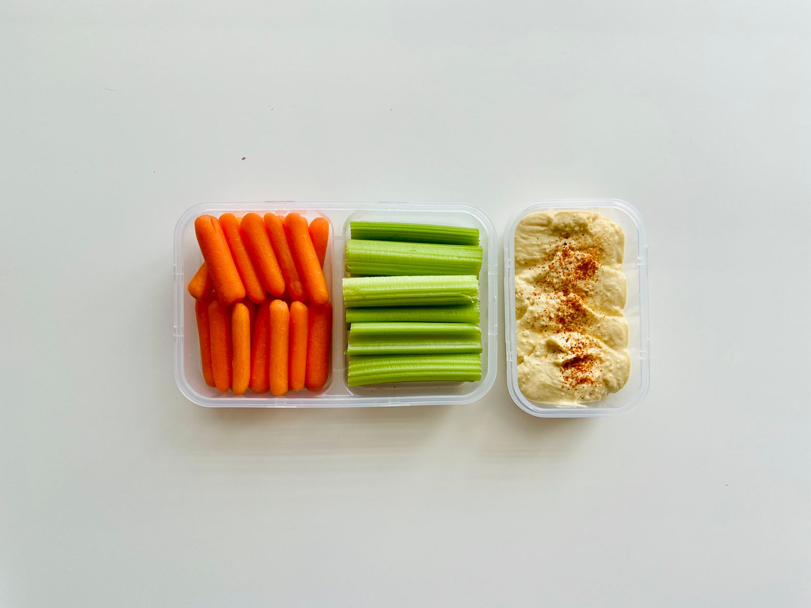 A cup of carrot and celery sticks with hummus