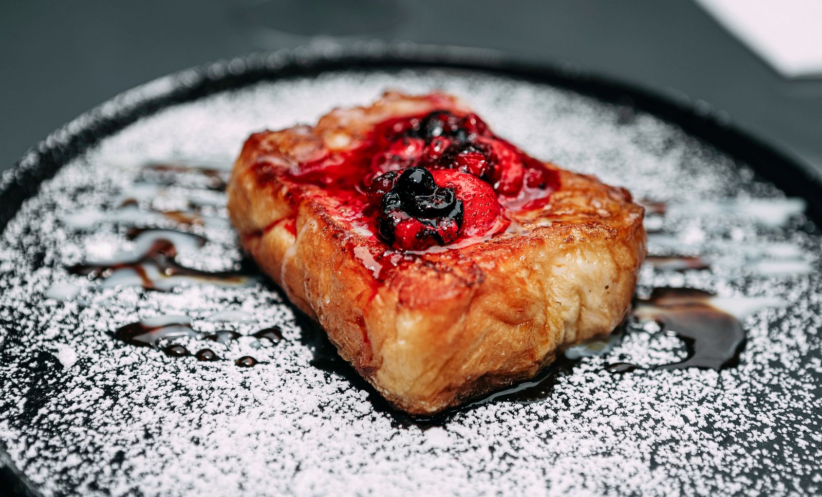 Thick slice of French toast topped with berries and powdered sugar