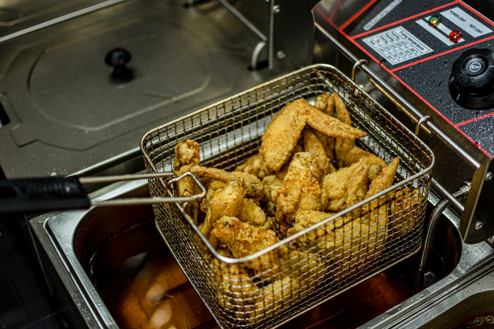 Golden fried chicken wings lifted from hot oil in a fryer basket