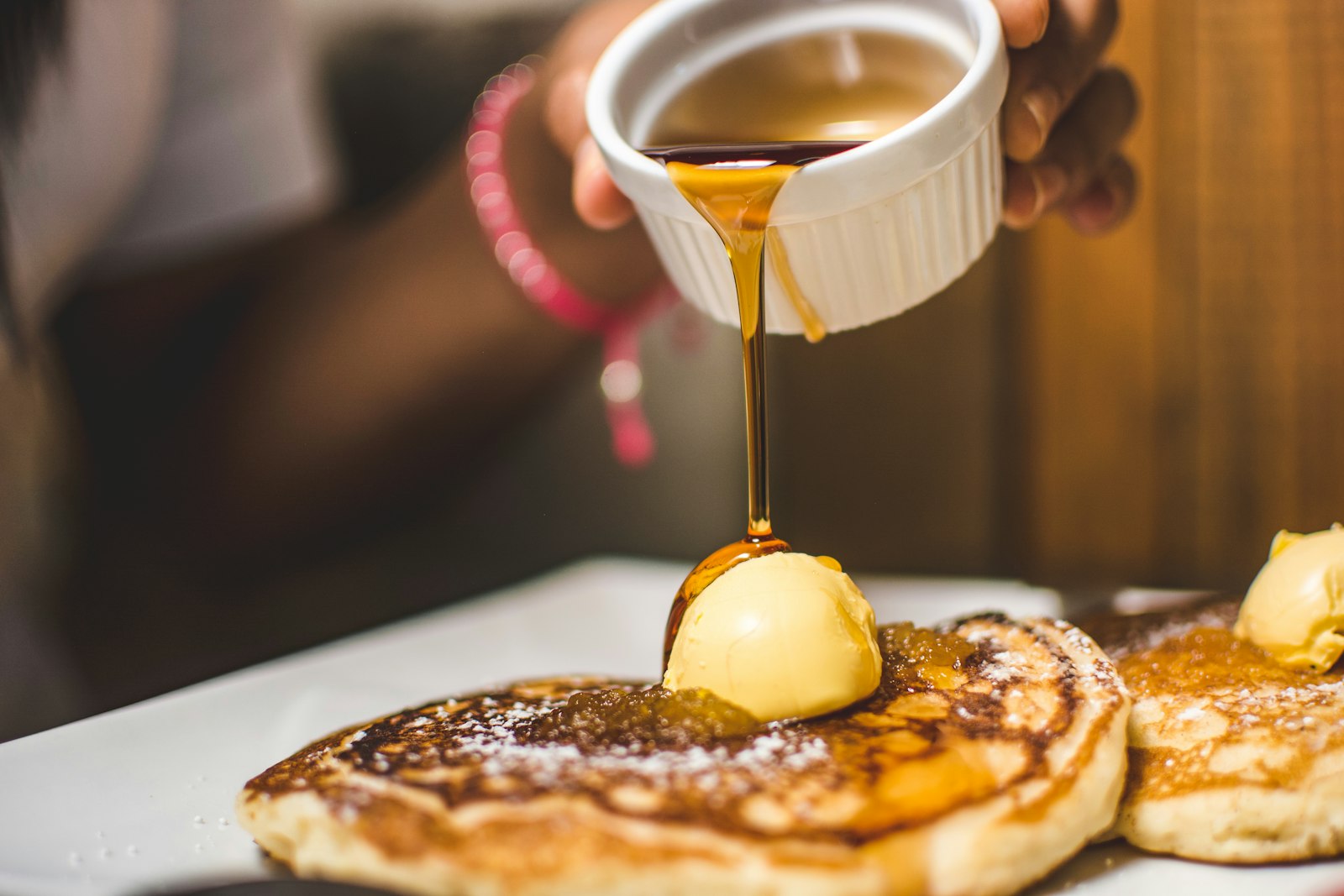 Syrup pouring over a stack of pancakes topped with butter