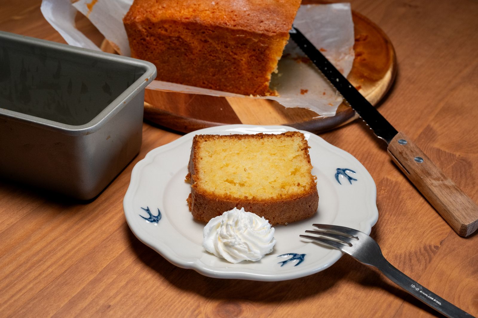 Slice of golden pound cake with whipped cream next to the loaf pan