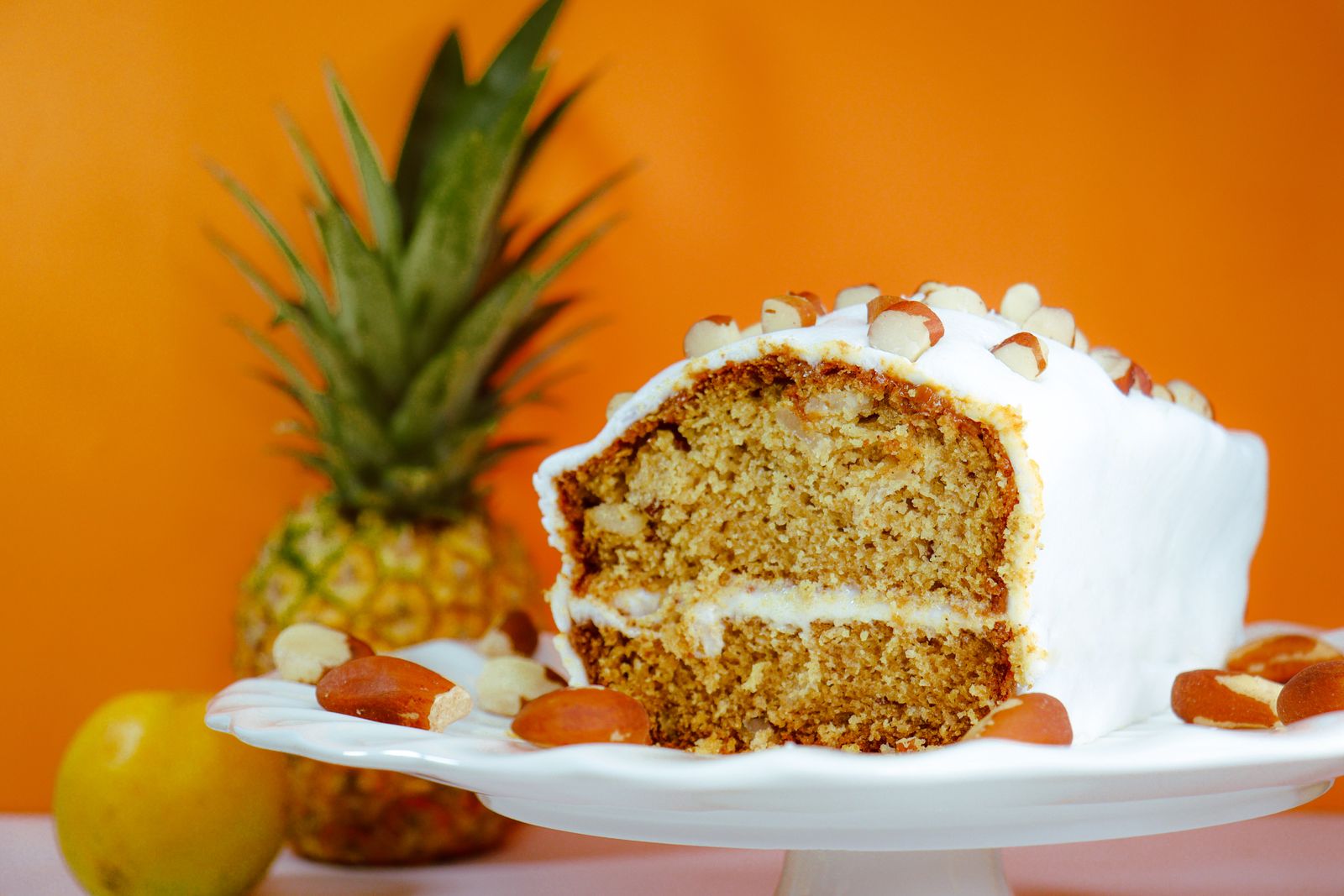 Slice of hummingbird cake with cream cheese frosting and a fresh pineapple