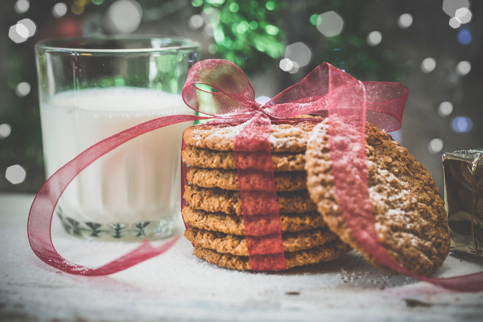 Stack of spice cookies tied with red ribbon next to a glass of milk, sweet holiday baking gifts