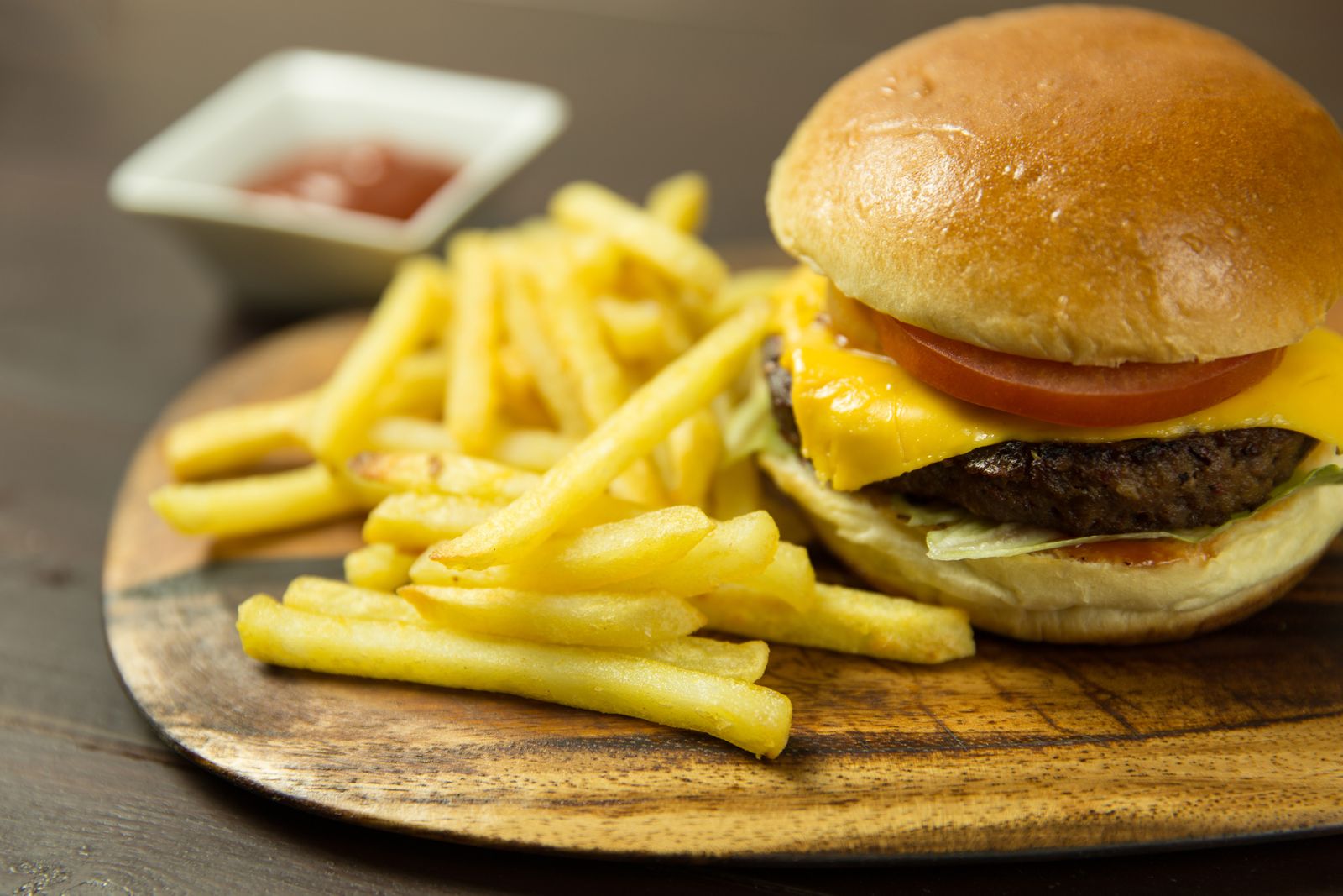 Cheeseburger with tomato and a pile of fries on a wooden board