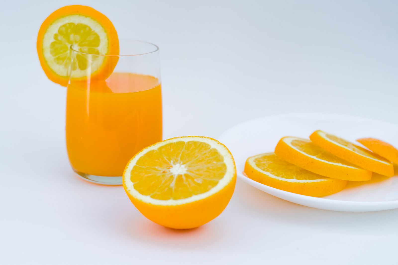 Glass of fresh orange juice next to orange halves and slices