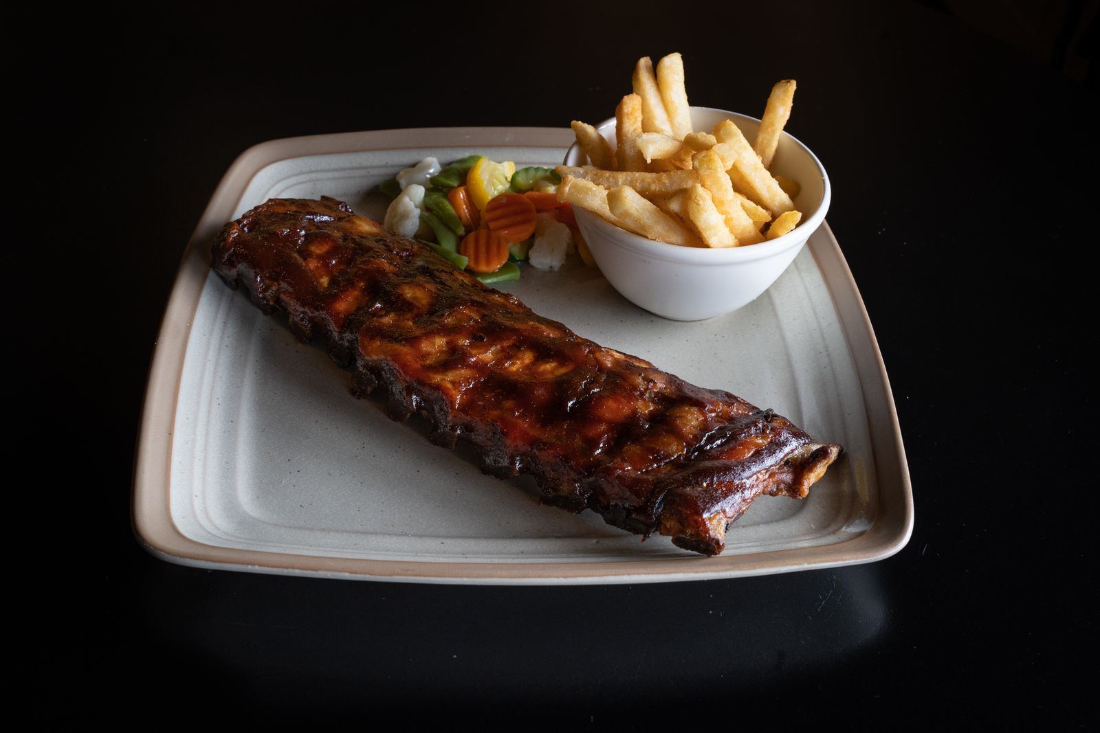 Oven baked pork spare ribs with fries on a white plate