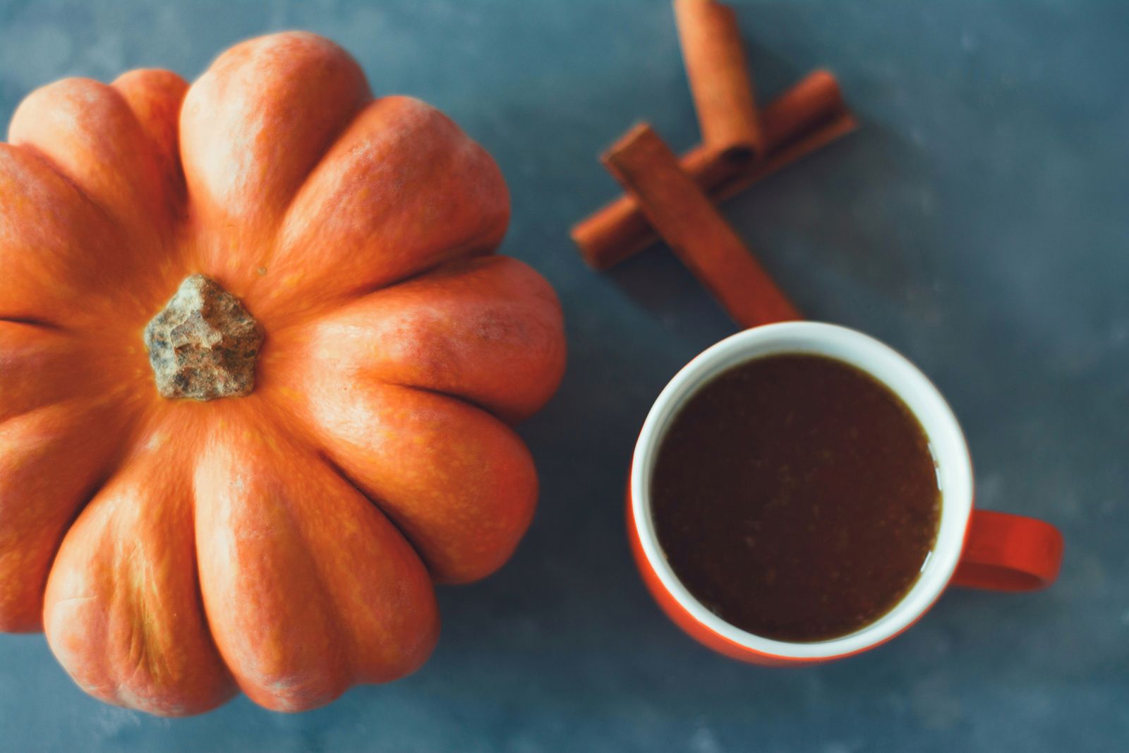 Cup of pumpkin spice coffee beside a pumpkin and cinnamon sticks