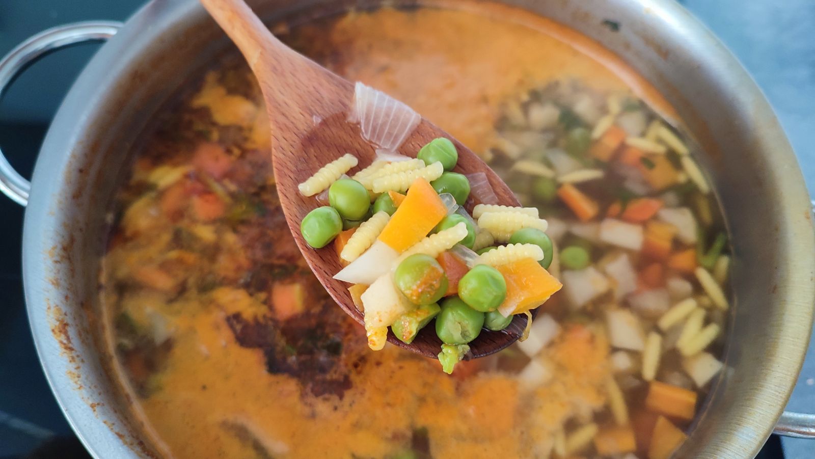 Wooden spoon lifting thick vegetable and pasta soup from the pot