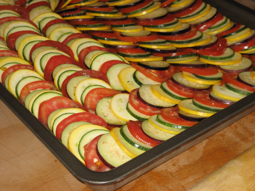 Rows of thin sliced vegetables in a big baking pan for ratatouille recipes for a crowd