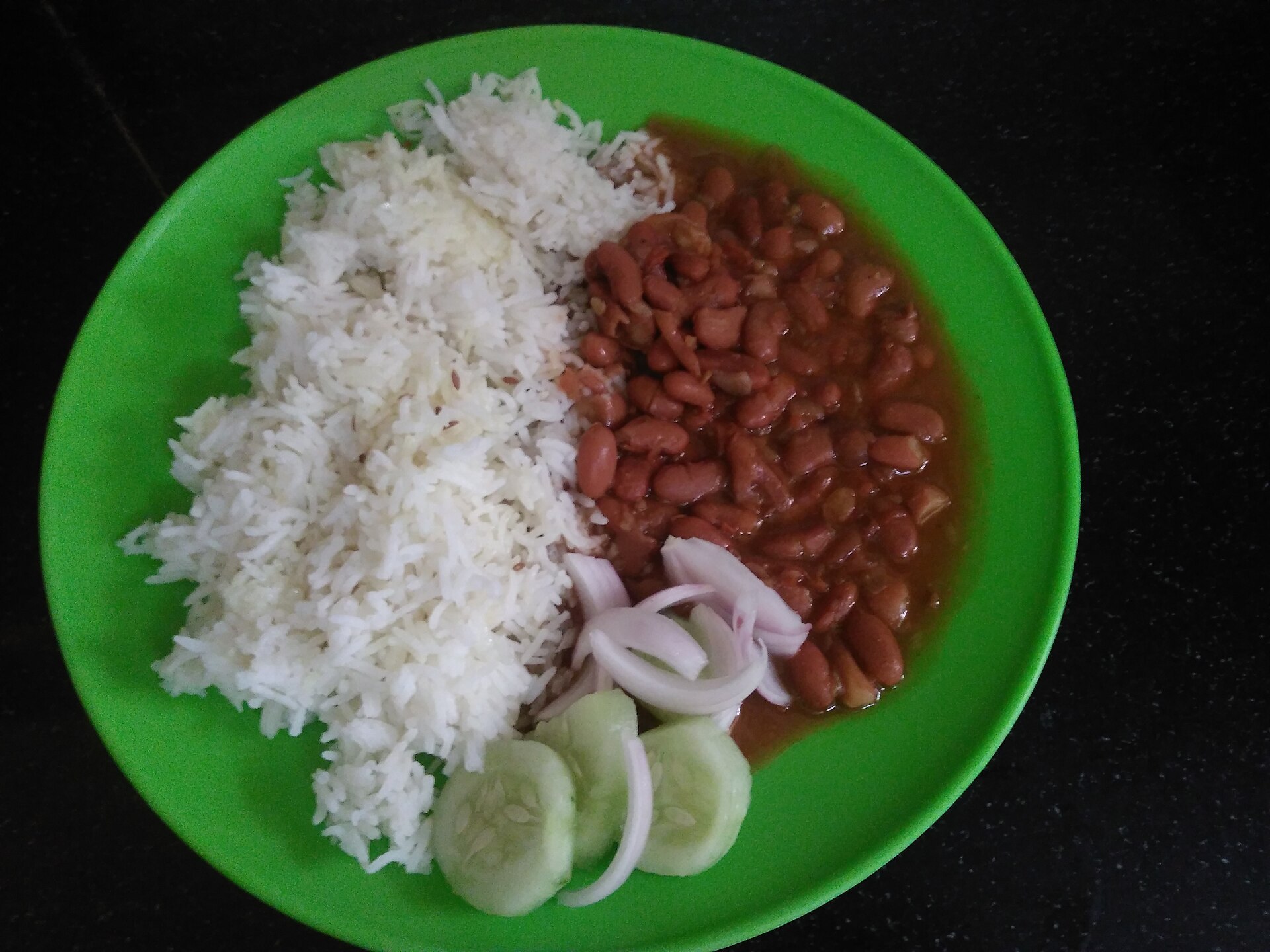 Plate of vegetarian red kidney beans and white rice with sliced onion and cucumber