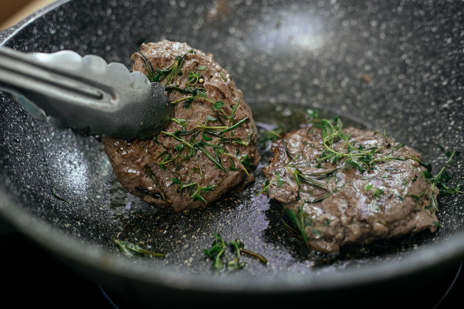 Salisbury steak patties browning in a black skillet with fresh rosemary