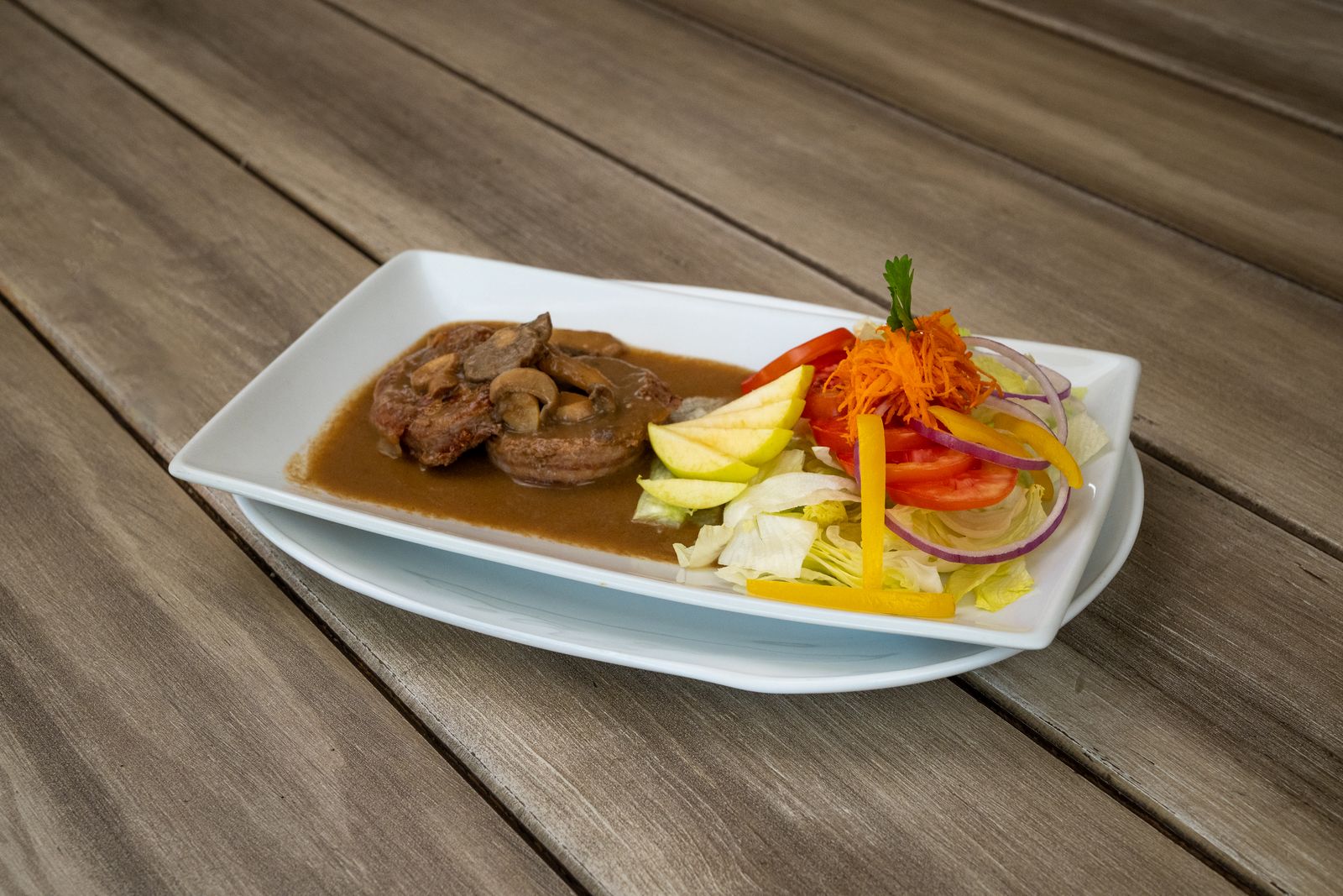 Beef patty in red wine mushroom sauce with a fresh salad on a white plate